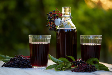 Glasses of fresh elderberry syrup and elderberries on a wooden table