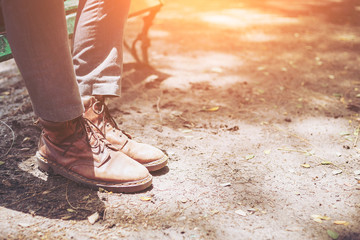 Naklejka premium Brown leather boots and wearing gray jeans of young fashion hipster man's legs with both feet stepped on the floor ground, concept of fashion and vintage lifestyle.