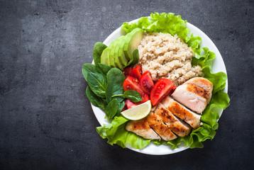 Fresh salad from quinoa, chicken breast, spinach, lettuce and tomatoes on black table
