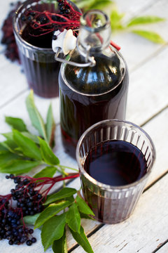 Glasses of fresh elderberry syrup and elderberries on a wooden table