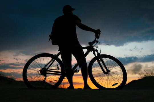Silhouette of cyclist on the background of sunset. Biker with bicycle on the sand during sunrise