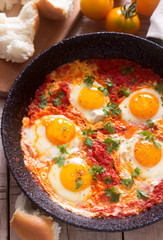 Shakshuka with bread on a wooden table. Middle eastern traditional dish. Homemade. Selective focus.
