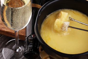 Gourmet Swiss fondue dinner on a winter evening with assorted cheeses on a board alongside a heated pot of cheese fondue with two forks dipping bread and white wine behind in a tavern or restaurant