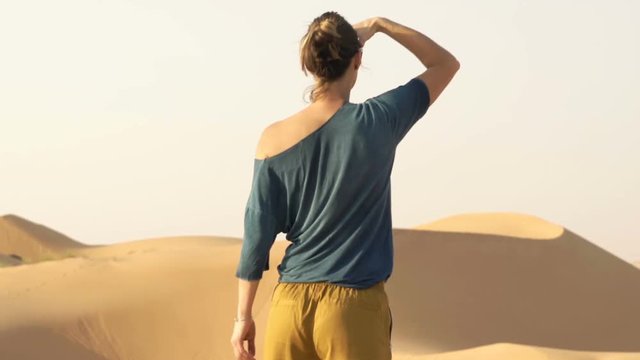 Unhappy, lost woman with hand searching direction walking on desert
