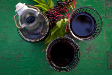 Glasses of fresh elderberry syrup and elderberries on a wooden table, top view