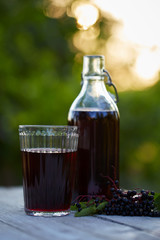 Glass of fresh elderberry syrup and elderberries on a wooden table