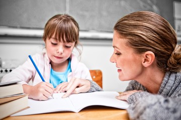 Schoolgirl writing with her teacher in classroom