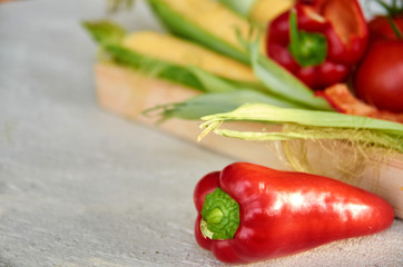 Red sweet bell pepper in the foreground on gray concrete surface close up. Fresh bell pepper and corn on blurred background. Side view