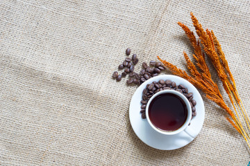coffee concept. coffee in white cup with roasted coffee bean and wooden spoon and red dried rice on sackcloth. copy space for text