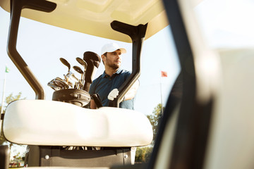 Golfer in cap standing at the golf cart