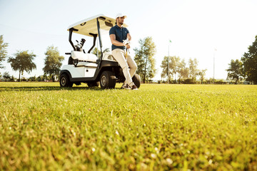 Young man resting while leaning on a golf cart