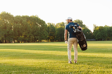 Back view of young man in cap carrying golf bag