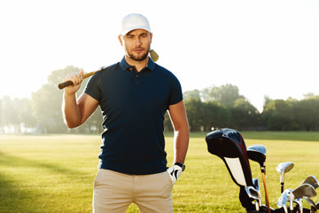 Handsome confident male golfer standing with golf club