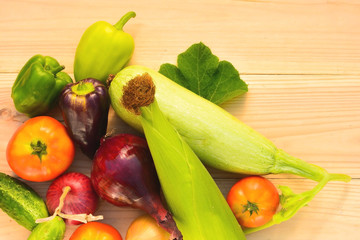 Green, purple peppers, tomatoes, corn, zucchini, blue and yellow onion on a wooden background in diffused light