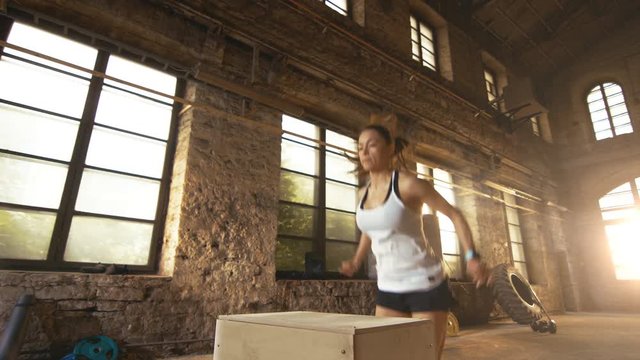 Fit Athletic Woman Does Box Jumps in the Deserted Factory Gym. Intense Exercise is Part of Her Daily Cross Fitness Training Program. Shot on RED EPIC-W 8K Helium Cinema Camera.
