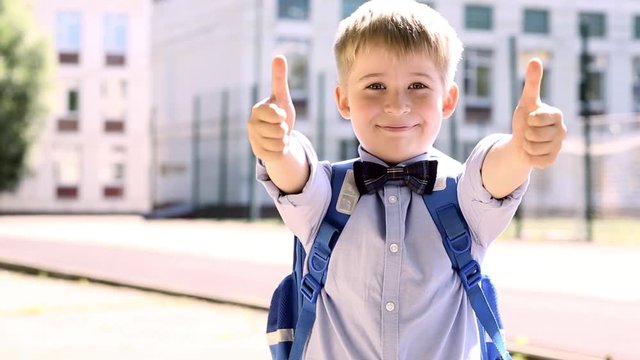   Funny child on the background of school. Smiling  boy  showing thumbs up sign.