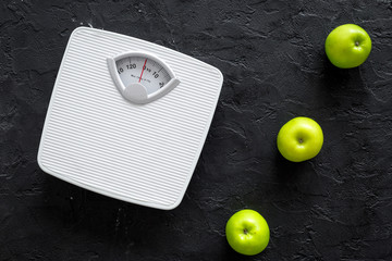 Diet for losing weight. Bathroom scale and apples on black background top view