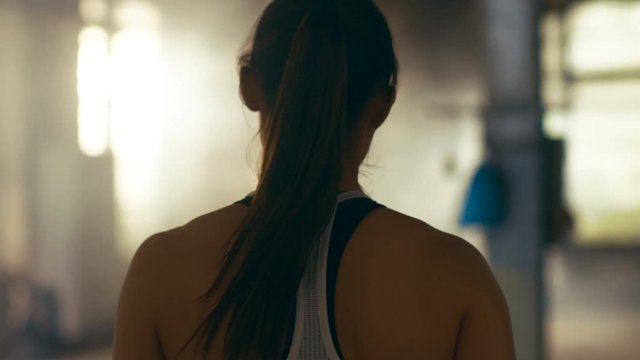 Follow-up Shot of Athletic Beautiful Woman Entering Gym in Slow Motion. She's Confident, Building is Industrial and Hardcore, Various Cross fitness/ Bodybuilding Equipment lying on the Floor. 