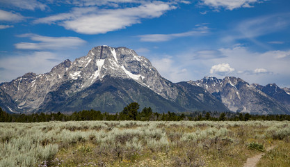 Fototapeta na wymiar The mountain peaks of Grand Teton National Park, Wyoming with glaciers and snow fields lake, blue color, sky, landscape with an active blue and cloudy sky