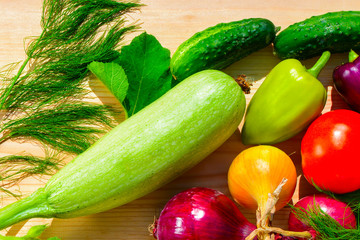 Green dill, purple peppers, tomatoes, zucchini, blue and yellow onion on a wooden background in sunlight