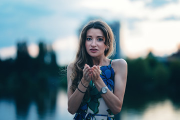 Teen girl standing in front of lake. Joining her palms and talking to her friend. Blonde curled...