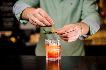 Bartender decorates cocktail with orange peel and rosemary close up