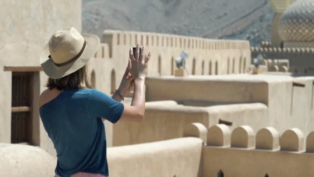Woman taking photo with cellphone of mosque in ancient fort in Oman
