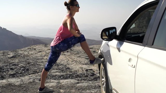 Young woman stretching legs on car tire near canyon
