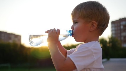 baby drinks water from bottle outdoors. Sunset time