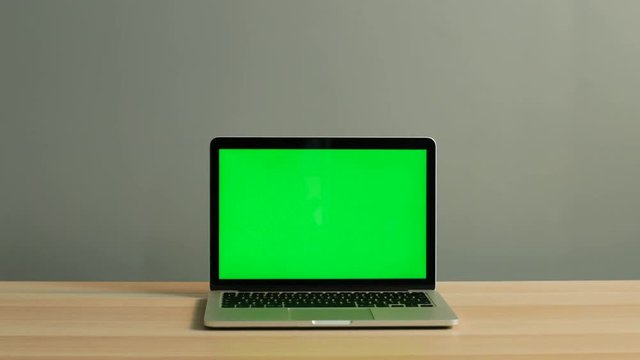 Close up shot of laptop with green screen on the light wooden table in the office. Chroma key.