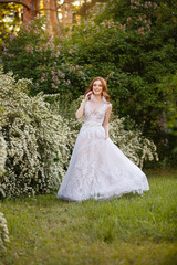 Fototapeta na wymiar Beautiful redhead Bride in blooming garden playing with her dress. Portrait outdoor in sunset light. Pretty young caucasian redhead girl