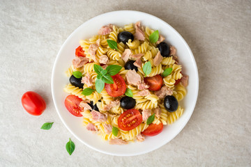 Fusilli pasta salad with tuna, tomatoes, black olives and basil on gray stone background