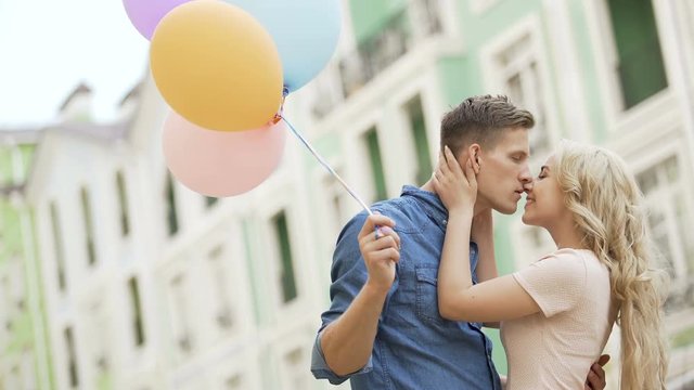 Couple walking down street, stopping to kiss, guy holding balloons, feelings