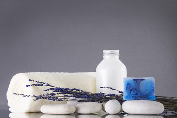 Fototapeta na wymiar Spa. The towel is rolled up, white pebbles, a bottle of cream. Lavender and blue soap. The background is gray.