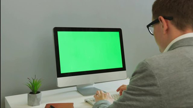 Back view of business man working on computer with green screen in the modern office. Chroma key.