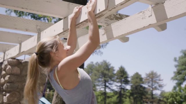 Friends Walk Together Through Pergolas In The Park (On Way To Yoga Class) Young Woman Jumps Up And Does A Pull-Up 