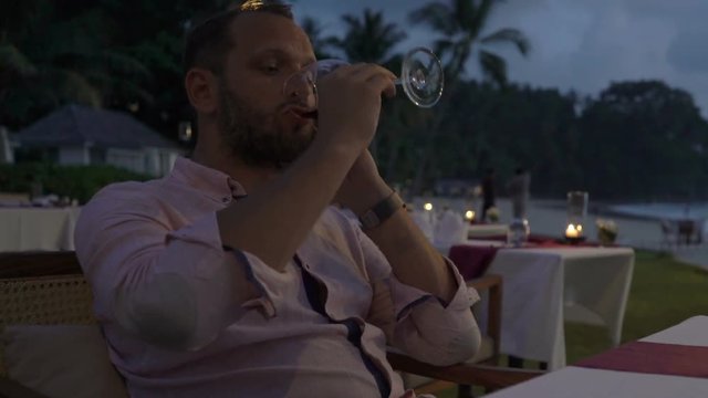Sad, unhappy man drinking wine in beach restaurant in evening

