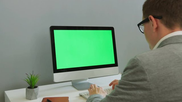 Back view of business man in the glasses working on computer with green screen in the modern office. Chroma key.