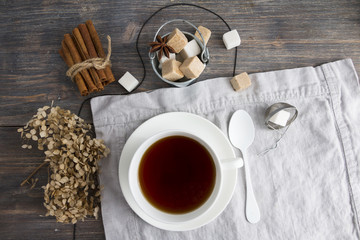 Cup of black tea on wooden table with cane and white sugar cubes, tea spoon and tea strainer. Top view.