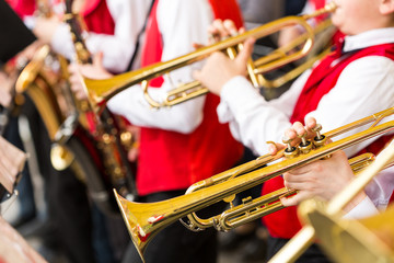 jazz band performance concept - orchestra of wind instruments during the variety show, selective focus on hands of musicians playing on trumpets and saxophones, closeup male in red concert costumes