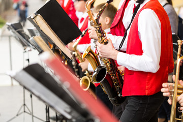 musical instrument, brass band and orchestra concept - festive performance of saxophones, closeup on sax and sheet music stands, musicians in red concert jackets and shirts, selective focus