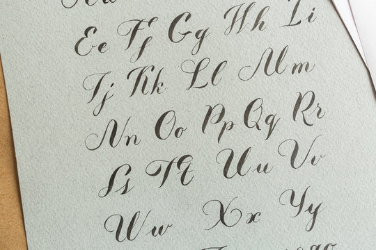 calligraphy, creation, hobby concept. italic letters of english alphabeth inscribing on the tough, coarse grey paper handwritten with night black ink in expressive, skillful manner
