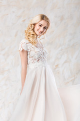 fashionable wedding dress, beautiful blonde model, bride hairstyle and makeup concept - stunning young woman in luxury white gown indoors on light background, pretty female posing with a smile