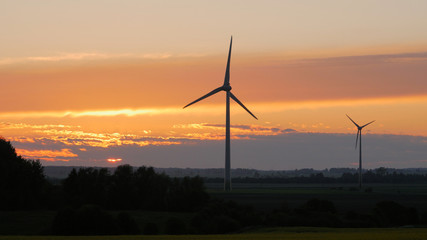 Wind turbines farms with rays of light at sunset in the background.