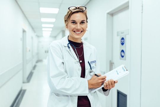 Happy young female doctor standing in hospital corridor