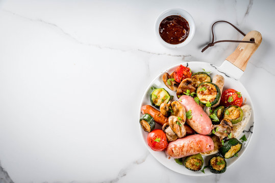 Barbecue. Assortment of various grilled meat sausages, with vegetables BBQ - mushrooms, tomatoes, zucchini, onions. On white marble table, on plate, with sauce. Copy space top view