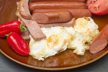 Fried eggs with sausage and bacon, a sausage cut in half
