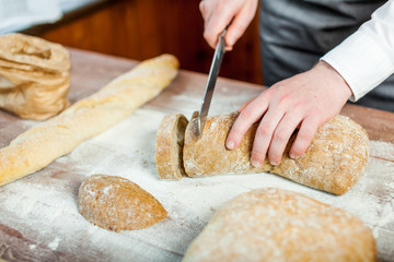 Male hands cutting fresh bread on the wooden table, selective focus