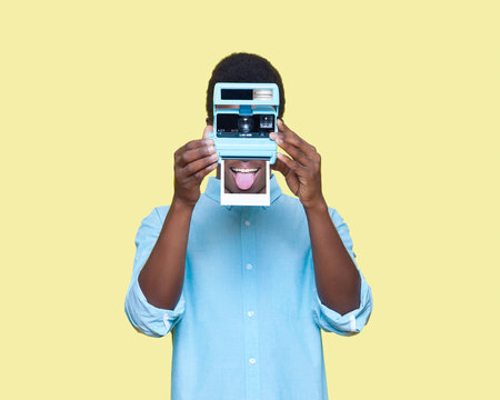 man holding instant camera, covering his face, on yellow background, conceptual