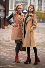 Two beautiful girls in an autumn coat. Two charming models in the center of the city.